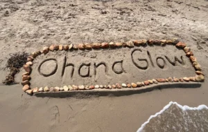 Nuestra filosofía de Ohana Glow escrita en la arena de la playa, origen natural de nuestra marca